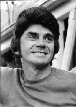 Headshot of a smiling man with thick, dark hair wearing a t-shirt