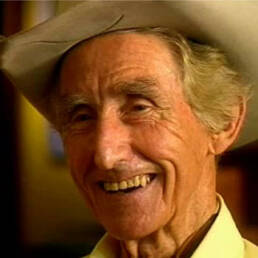 Headshot of a smiling elderly man wearing a cowboy hat and white collared shirt