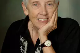 Headshot of a grey-haired woman wearing a black blouse, scarf, and watch resting her chin on her hand
