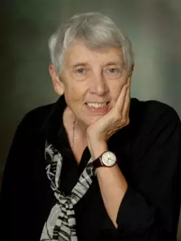 Headshot of a grey-haired woman wearing a black blouse, scarf, and watch resting her chin on her hand