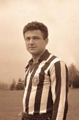 Man with short curly hair wearing a striped sports jersey standing on a playing field