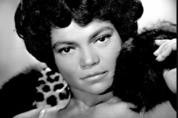 Black and white headshot of a woman wearing a sequin dress, fur on her shoulders and hair in a beehive style