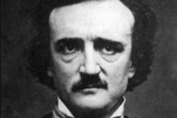 Black and white headshot of a man with dark bushy hair and a mustache wearing a high collared shirt