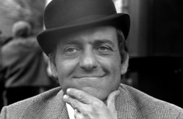 Headshot of a smiling man wearing a top hat and suit with his hand on his chin