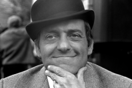 Headshot of a smiling man wearing a top hat and suit with his hand on his chin