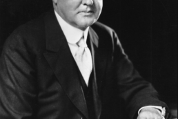 Older man wearing a suit and waistcoat seated and resting an arm on a table