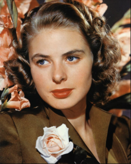 Headshot of a woman with dark curly hair wearing a brown button up blouse with a pink rose corsage