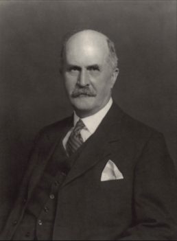Black and white headshot of a balding older man with a mustache wearing a suit, waistcoat and handerchieve