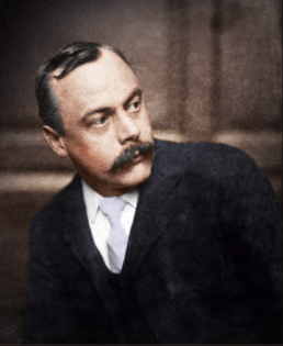 Headshot of a middle-aged man with a moustache wearing a suit and looking away from the camera