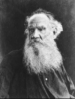 Black and white headshot of a balding elderly man with a long beard and mustache wearing a black button-up shirt