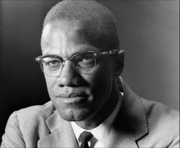 Black and white headshot of a short-haired man with a neutral expression in a suit and glasses