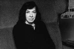 A dark-haired middle age woman wearing a black shirt and sitting in an armchair