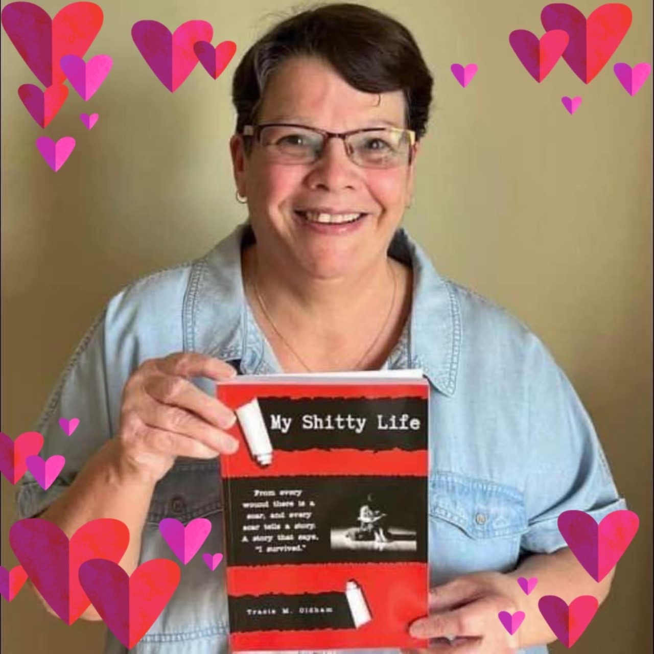 Hearts photoshopped around a smiling woman with brown short hair wearing glasses and holding up a book titled 