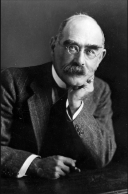 Black and white headshot of a bald man with a bushy mustache and glasses resting his head on his chin