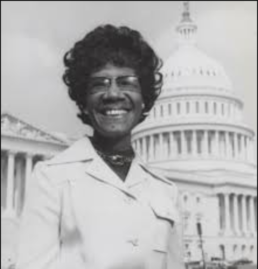 Black and white headshot of a smiling woman wearing glasses and a trenchcoat in front of the US Capitol