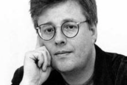 Black and white headshot of a middle-aged man with glasses resting his hand on the side of his face