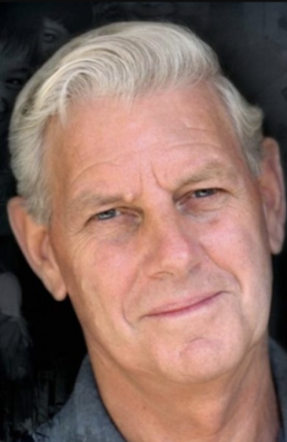 Headshot of a grey-haired man with his head tilted at an angle with a neutral facial expression