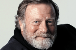 Headshot of a smiling man with grey hair and a beard wearing a black turtleneck shirt