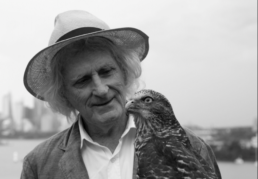 Black and white headshot of an older man wearing a hat looking at a large bird