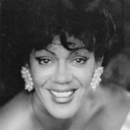 Black and white headshot of a smiling woman wearing large pearl earrings and a strapless top