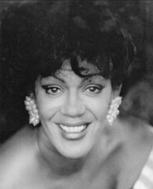Black and white headshot of a smiling woman wearing large pearl earrings and a strapless top