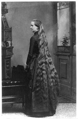 Black and white image of a lady with very long hair wearing an old fashioned dress.