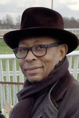 Headshot of a smiling man with glasses wearing a tophat and coat in front of a white fence