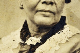 Black and white photo of a woman with short, curly black hair wearing earrings and a dress with a lacy collar.