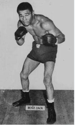 Black and white image of a muscular, shirtless man with an Afro wearing boxing clubs in a fighting stance