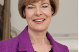 Headshot of a smiling woman with a brown bob wearing a magenta suit jacket and black blouse